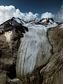 Aerial view of the Presena Glacier cascading down the mountainside under a dramatic sky, the stark white ice contrasting against the rugged, brown terrain, Brescia, BS, Italia.