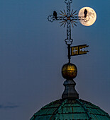 Aerial view of a full moon glowing behind a cross atop a building with a flag, Cathedral, Lugano, Switzerland