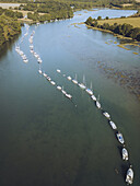Aerial view of boats lined up in the channel, reflecting the sunlight, between lush green banks, creating a captivating contrast of blue and green, Vannes, Bretagne, France.