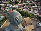 Luftaufnahme der leuchtend blauen Kuppel einer Moschee, die mit den Erdtönen der umliegenden Gebäude kontrastiert und einen eindrucksvollen visuellen Wandteppich bildet, Samarqand, Samarqand viloyati, Usbekistan.