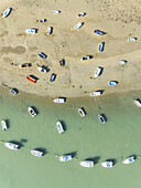 Aerial view of boats scattered on the sandy shore meeting the tranquil sea, a dance of vibrant hues under the sun, Sancti Petri, Bay of Cádiz, Cádiz province, Andalusia, Spain.