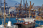 Luftaufnahme von riesigen Kränen, die über Frachtschiffe im geschäftigen Hafen wachen, eine Symphonie der Industrie vor azurblauem Hintergrund, Piräus, Griechenland.