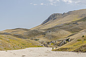 Blick auf sonnenverwöhnte Täler und zerklüftetes Gelände, die sich unter einem heiteren Himmel zu einem Tableau natürlicher Schönheit zusammenfügen, Isola del Gran Sasso D'italia, Abruzzen, Italien.