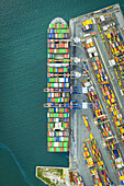 Luftaufnahme eines riesigen Containerschiffs, das an einem Kai angedockt ist, der mit Stapeln von bunten Containern gefüllt ist, ein pulsierender Tanz von Handel und Industrie, La Spezia, Ligurien, Italien.