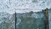 Luftaufnahme von krachenden Wellen, die auf das ruhige Wasser eines Ozeanpools treffen, Kontrast zwischen dem wilden Meer und der von Menschenhand geschaffenen Struktur, Sydney, Australien.