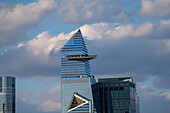 Blick auf einen modernen Wolkenkratzer, der den Himmel durchdringt, dessen scharfe Winkel und Glasfassade das wechselnde Licht unter einem bewölkten Himmel reflektieren, Hudson Yard, New York, Vereinigte Staaten.