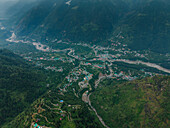 Aerial view of the lush green valley floor contrasting with the rugged mountain terrain, where the Beas River winds through, Manali, Himachal Pradesh, India.