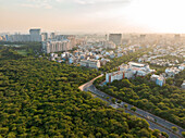 Aerial view of a city skyline meeting a lush green forest along the winding roads of Sunset Boulevard, Gurugram, Haryana, India.