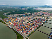 Aerial view of a vast, colorful port sprawling with stacked containers under a hazy sky, contrasting with the calm, reflective water at Jawaharlal Nehru Port Trust (JNPT) in Navi Mumbai, India