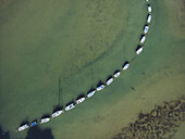 Aerial view of boats lined up in a curve on the water, contrasting with the sandy seabed and green water, Presqu'île de Conleau, Bretagne, France.