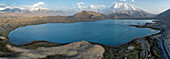 Aerial view of turquoise waters meet rugged shores under the gaze of snow-capped Muztagh Glacier, Karakul Lake, China.