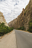 View of the asphalt road winding through the rugged, towering cliffs under a sky streaked with clouds, creating a dramatic scene, Areni, Vayots Dzor Province, Armenia.