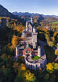 Das majestätische Schloss Neuschwanstein erhebt sich aus der Vogelperspektive inmitten eines farbenprächtigen Herbstlaubteppichs, eingerahmt von fernen, dunstigen Bergen, Schwangau, Bayern, Deutschland.