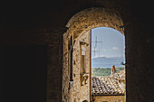 View of rustic stone archway framing distant mountains and tile rooftops under a bright, clear sky, Santo Stefano di Sessanio, Abruzzo, Italy.