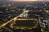 Aerial view of a brightly lit stadium near Club Road, its vibrant green field contrasting with the surrounding cityscape under the twilight sky, Kano, Kano, Nigeria.
