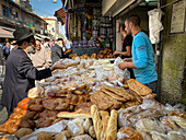 Jerusalem, Israel - 01 November 2019: View of the bustling market scene with a vendor selling an assortment of breads to a customer, a symphony of golden hues and textures under the bright daylight.