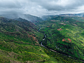 Aerial view of a river winding through the verdant, rugged landscape under a moody, overcast sky, Waimea Ditch, Hawaii, United States.