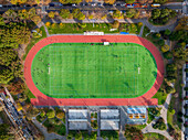 Aerial view of a vibrant green sports field encircled by a red running track, nestled among autumn trees, their leaves a mosaic of gold and russet, , Brooklyn, New York, United States.