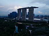 Aerial view of the iconic Marina Bay Sands piercing through the skyline, juxtaposed against the dark, lush greenery of Gardens by the Bay, Singapore, Singapore.