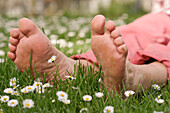 Entspannte nackte Füße auf Frühlingswiese mit Gänseblümchen