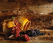 Schwarze und rote Weintrauben mit Tontöpfen vor Holzuntergrund