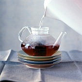 Heisses Wasser aus dem Wasserkocher in eine Glaskanne mit Tee gießen
