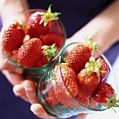 Hand hält zwei Gläser mit Erdbeeren