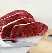 Rohe Rindfleisch-Scheiben mit Messer und Papier auf Schneidebrett