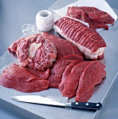Verschiedene Fleischstücke vom Rind mit Küchengarn und Messer auf einem Blech