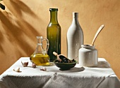 Oliven-Stillleben mit Öl in Flaschen und Karaffe, Oliven und Knoblauch