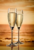 Zwei Gläser Champagner, im Hintergrund Sonnenuntergang in Sepia
