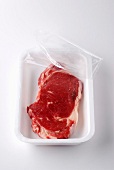 Raw steak in plastic container
