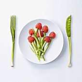 Sinnbild für gesunde Ernährung: Besteck aus Gemüse neben Teller mit Himbeeren und Bohnen