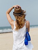 Junge Frau am Strand trägt blaue Wasserflaschen über der Schulter