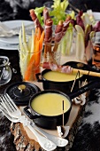 Individual cheese fondues with bread sticks wrapped in Parma ham and raw vegetables