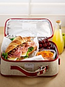 Croissant sandwich with raw carrot and grapes in a lunch box