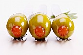 Three green olives stuffed with red peppers on forks