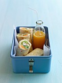 Chicken and vegetable wraps and orange juice in a lunch box