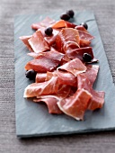 Sliced Aoste ham and olives on slate