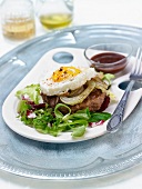 Hamburger topped with a fried egg, barbecue sauce and salad