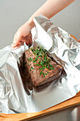 Wrapping the roast beef with herbs in a sheet of aluminium foil
