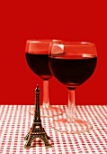 Zwei Gläser Rotwein mit kleinem Eiffelturm auf karierter Tischdecke