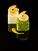 White and green risotto cubes topped with king prawns on a black background