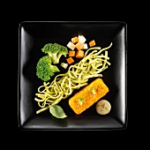 Vegetarian dish of noddles with pesto,pureed carrots and crisp vegetables on a black background