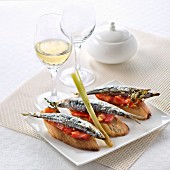 Bruschetta mit gebratenen Sardinen, Tomaten und Zitronengras, Glas fruchtiger Weißwein