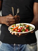 Person holding a plate of watercress and mixed vegetable salad