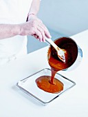 Pouring the caramel into a shallow tin mould coated with wax paper