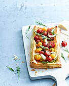 Overhead view of tomato and parmesan puff pastry tart garnished with rocket on cutting board