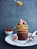 Pouring honey on a stack of plain pancakes and chocolate pancakes with quarters of figs