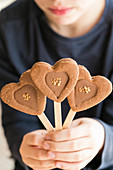 Child holding heart-shaped chocolate biscuits on sticks
